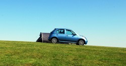 A Car parked in a field, with a Tent just behind.